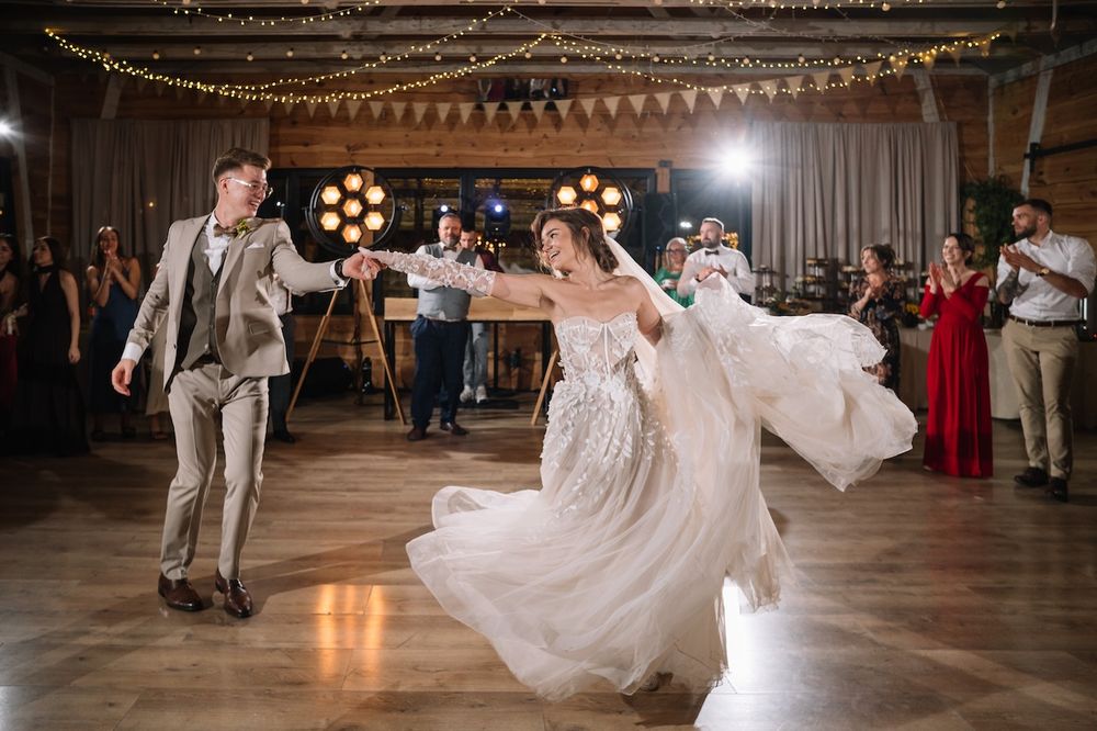 Bride in flowing white gown and groom dancing energetically at their wedding reception.