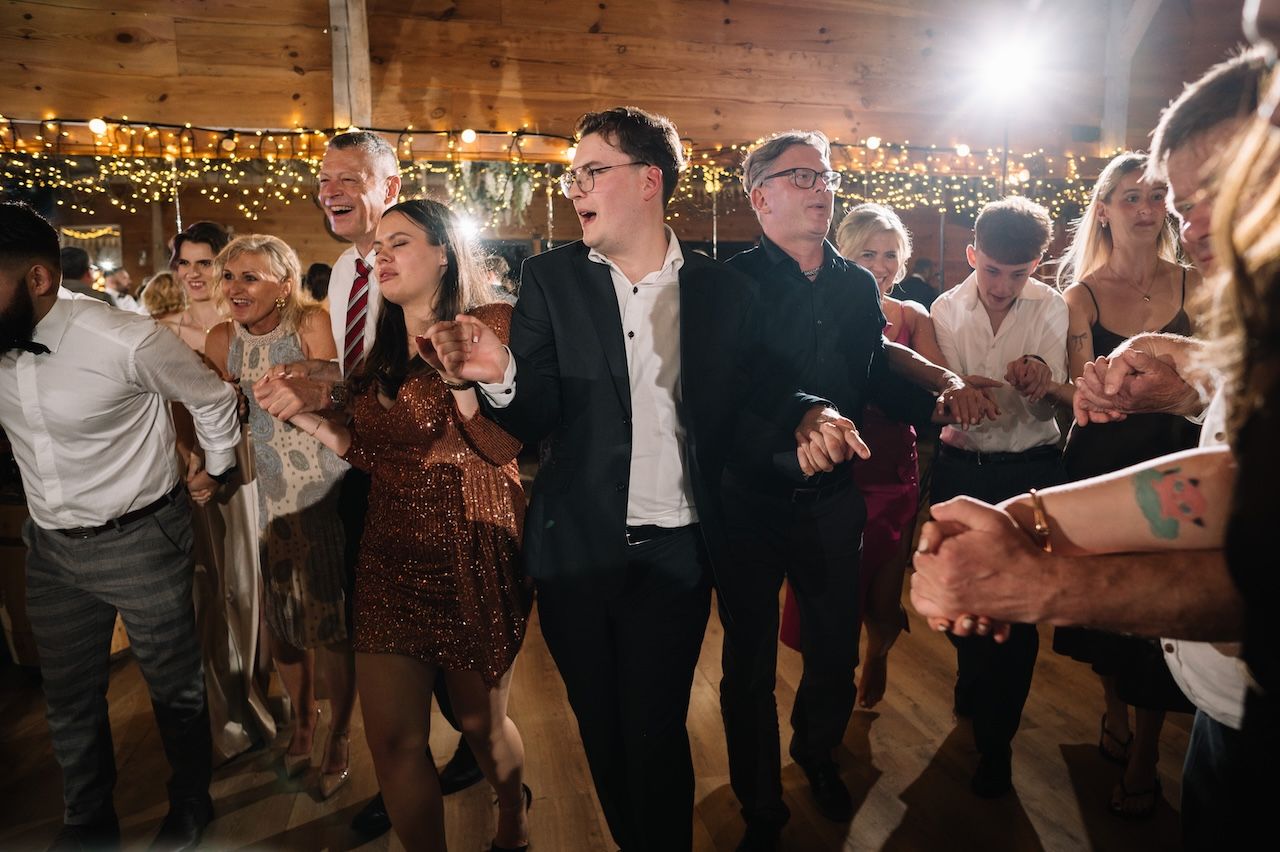 Guests dancing joyfully at a rustic wedding reception with warm string lights in the background.