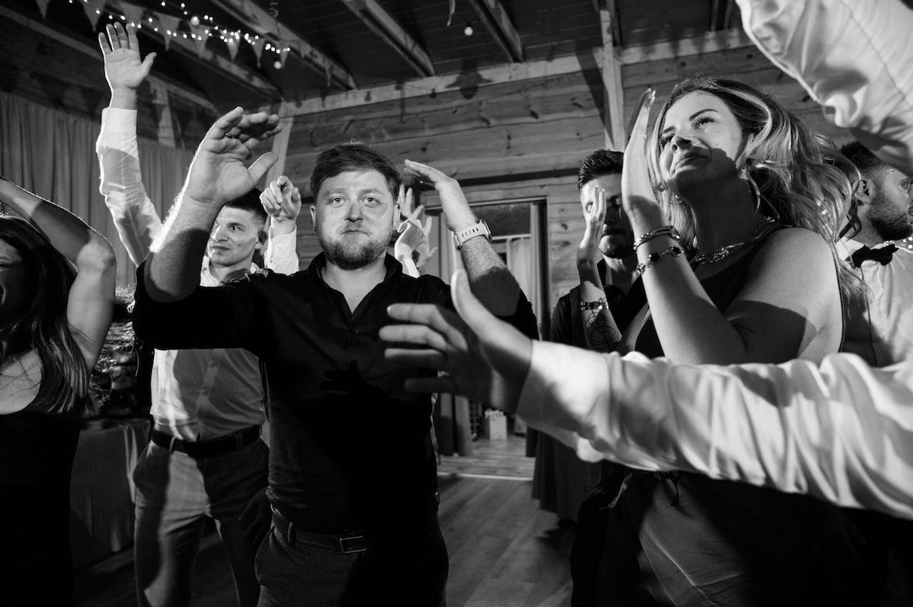 Black and white photo of a man dancing energetically at a lively wedding reception.