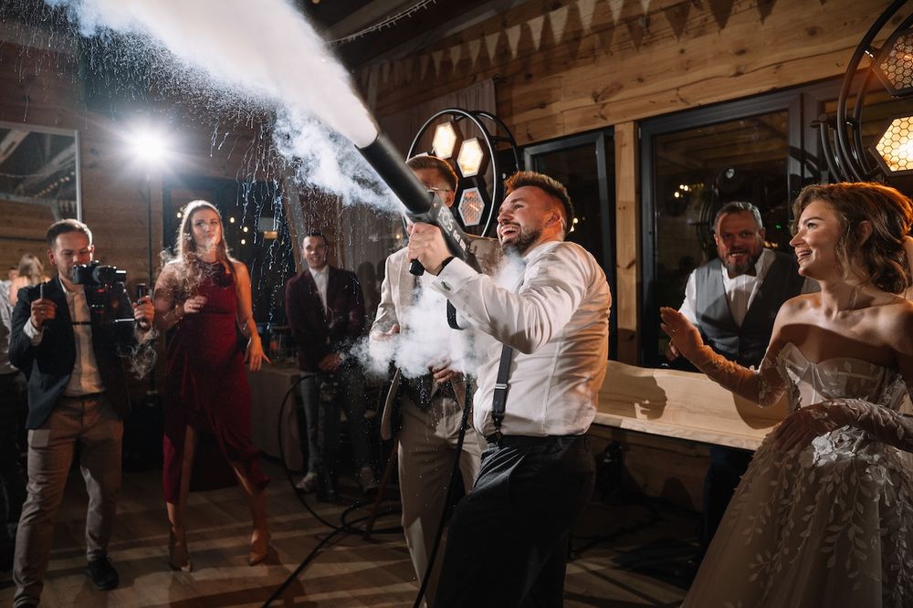 Groomsman firing a confetti cannon at a festive wedding reception while guests celebrate.