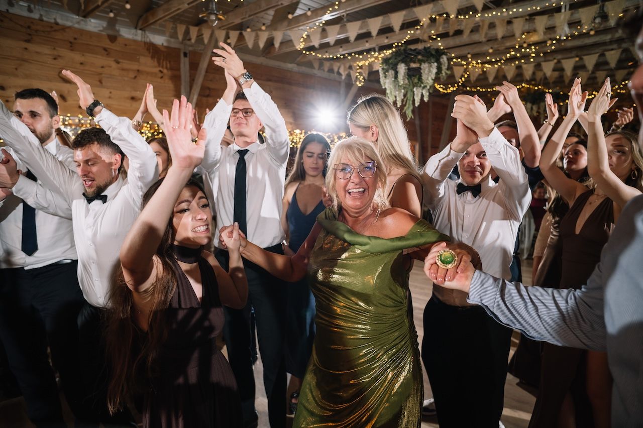 Guests dancing enthusiastically at a wedding reception in a rustic barn with string lights.