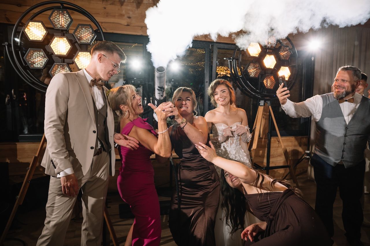 Wedding guests laughing and celebrating together near vintage industrial lighting at a reception.