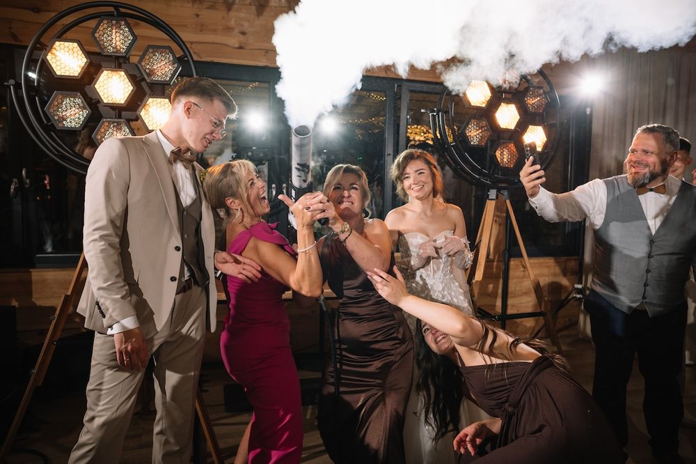 Wedding guests laughing and celebrating together near vintage industrial lighting at a reception.