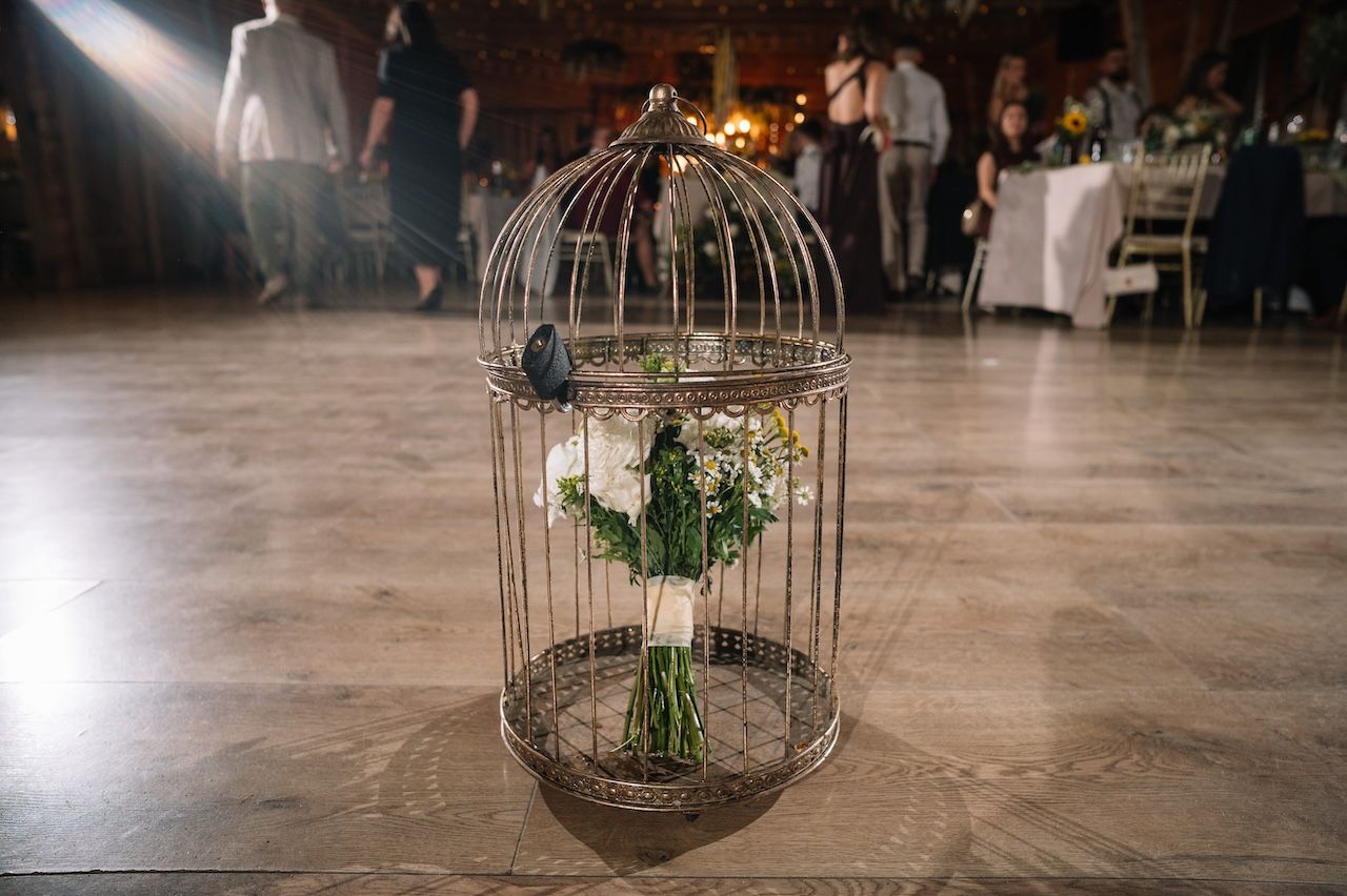 Bridal bouquet of white flowers displayed inside a decorative birdcage on a dance floor.