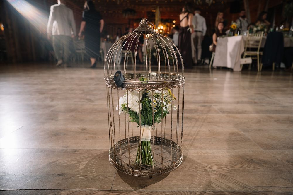 Bridal bouquet of white flowers displayed inside a decorative birdcage on a dance floor.