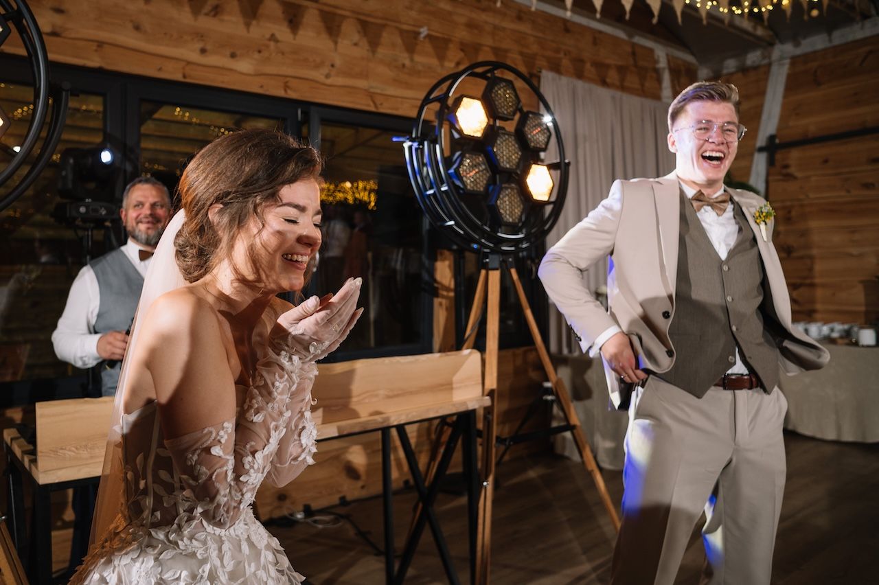 Bride and groom laughing joyfully together at rustic barn wedding reception with stage lighting.