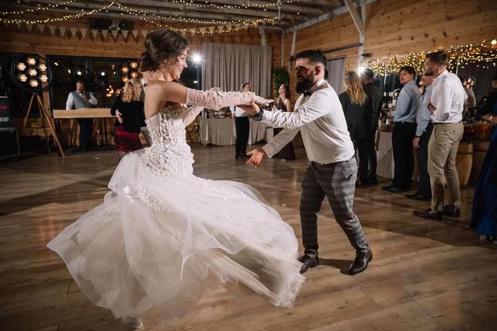 Bride in lace gown spinning with groom on dance floor at romantic barn wedding.