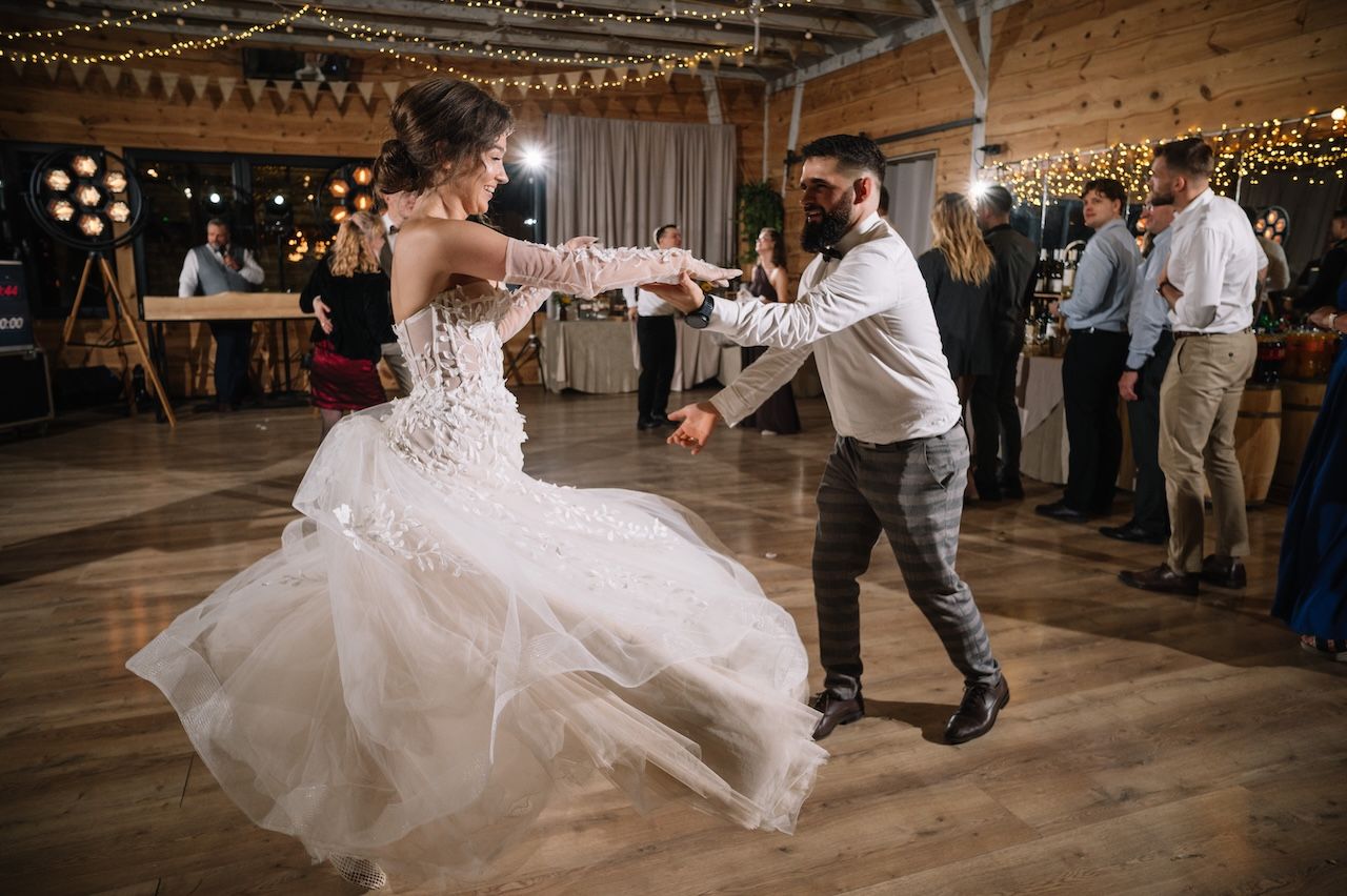 Bride in lace gown spinning with groom on dance floor at romantic barn wedding.