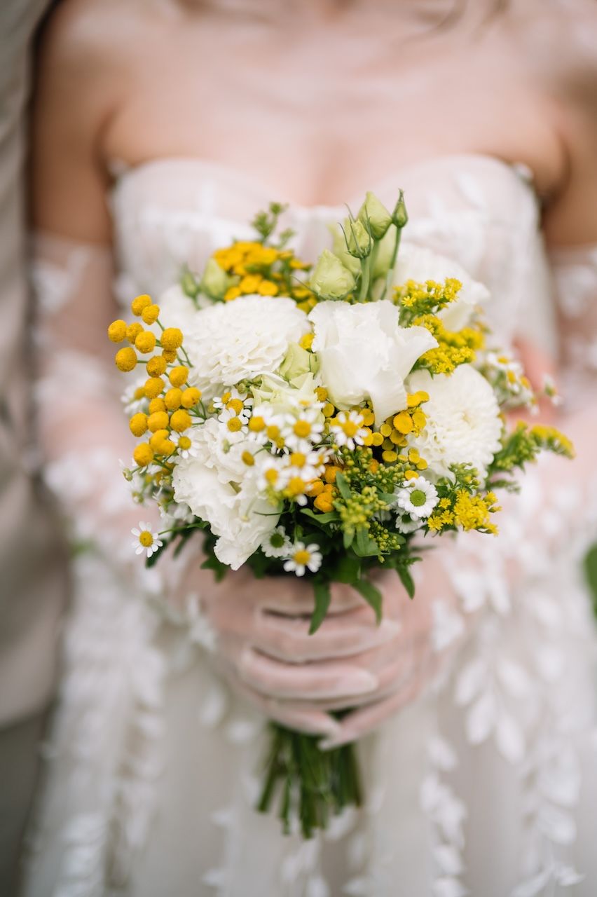 Close-up of a bridal bouquet featuring white and yellow wildflowers held by a bride.