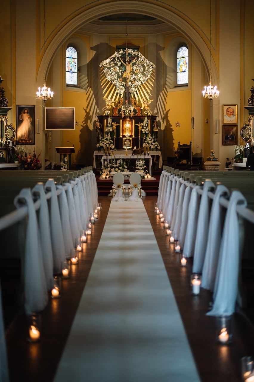 Church aisle decorated with white draping, candles, and floral arrangements leading to ornate altar.