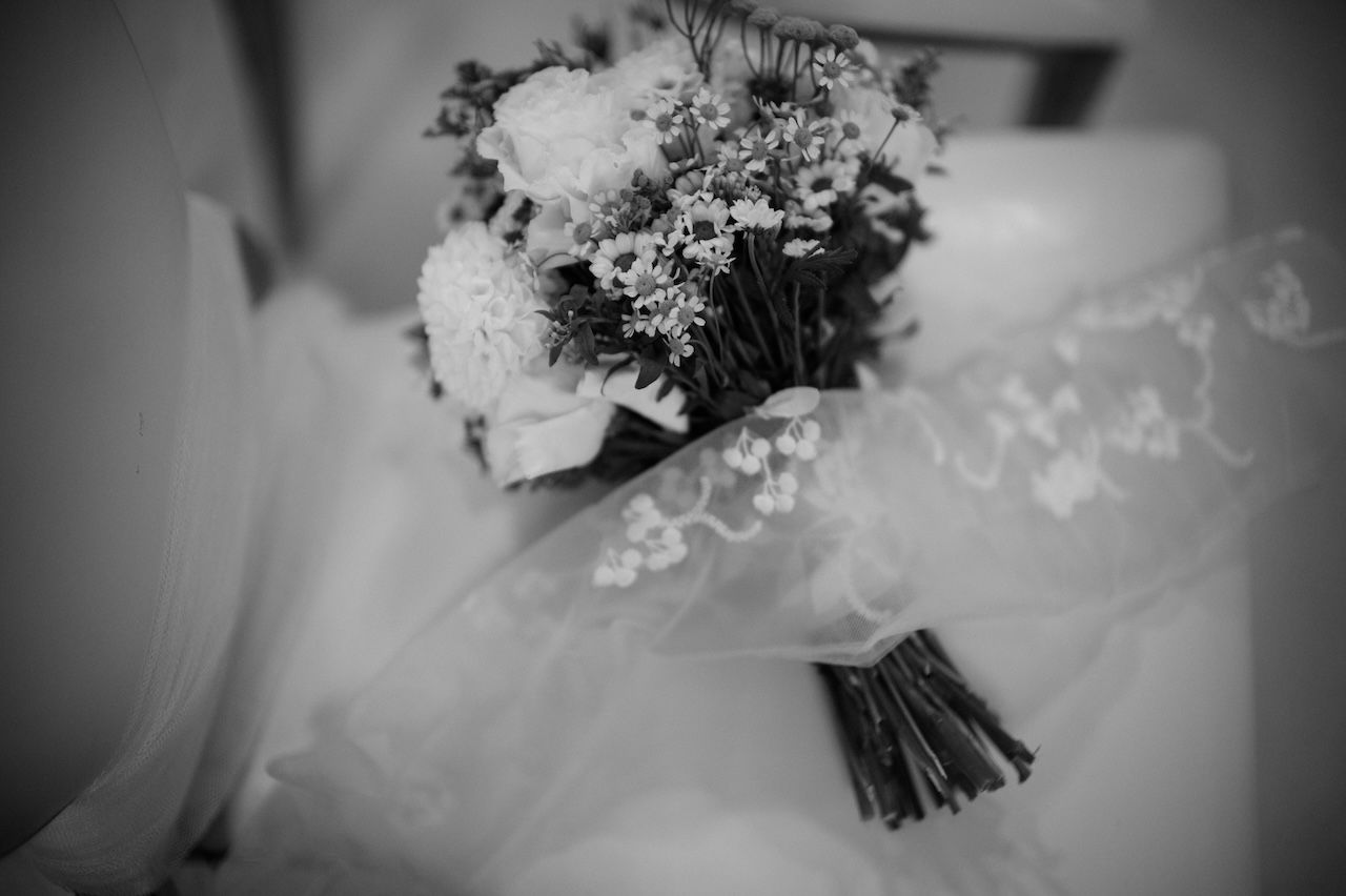 Black and white close-up of bridal bouquet wrapped in lace veil fabric.