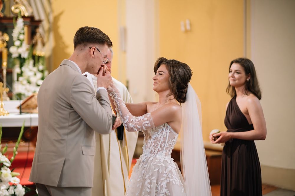 Emotional groom wiping tears as bride tenderly touches his face during wedding ceremony.
