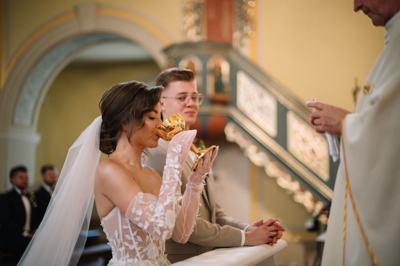 Bride and groom receiving communion from golden chalices during Catholic wedding ceremony.