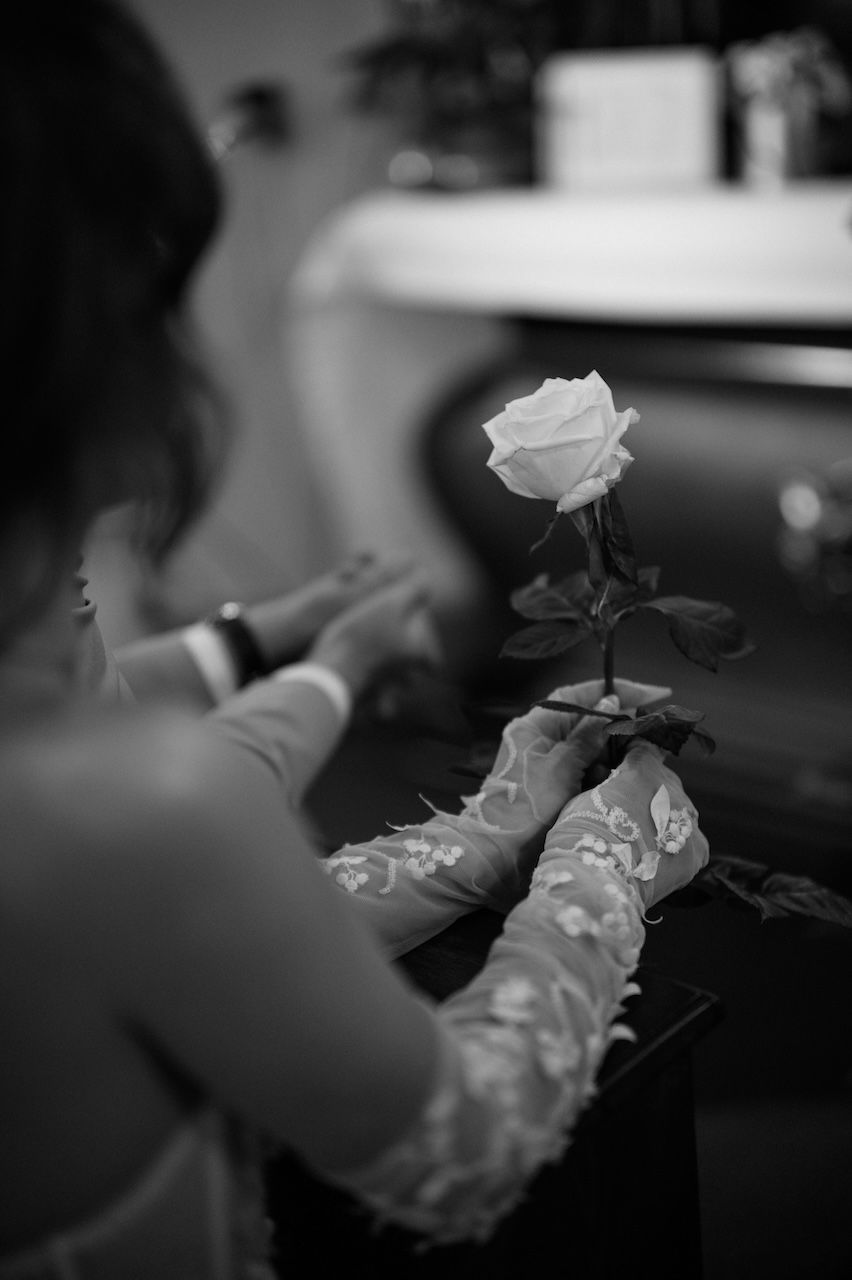 Black and white close-up of bride holding a single white rose during wedding ceremony.