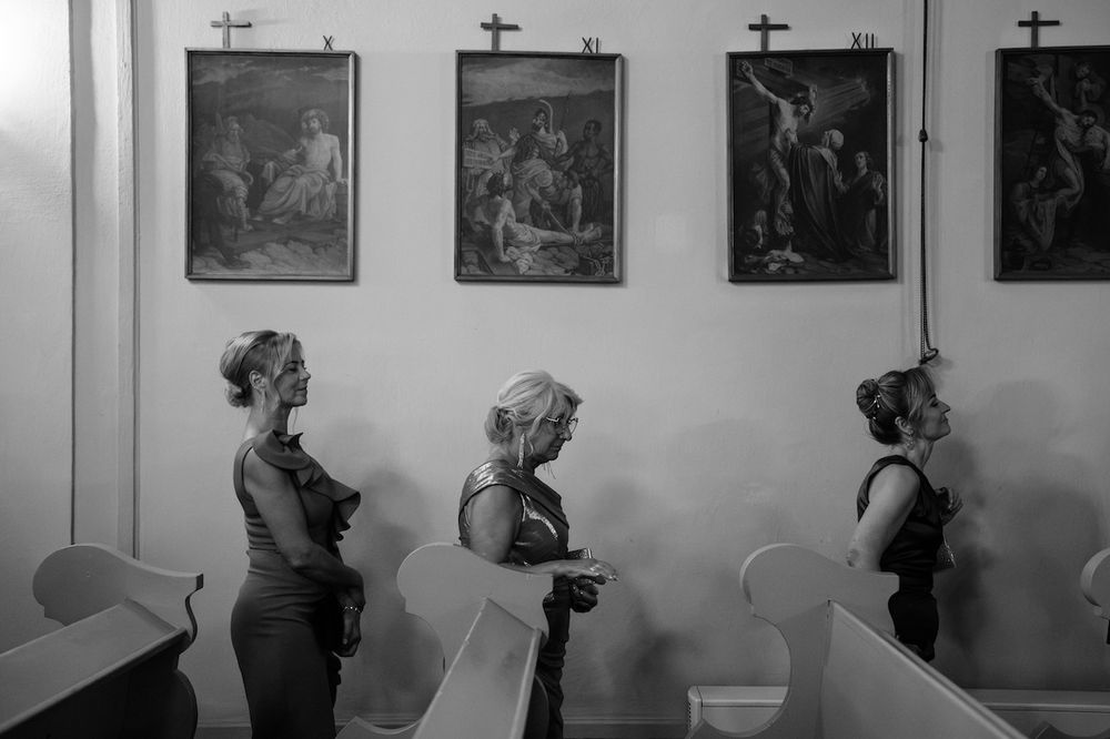 Black and white photo of women standing by church pews beneath religious paintings on wall.