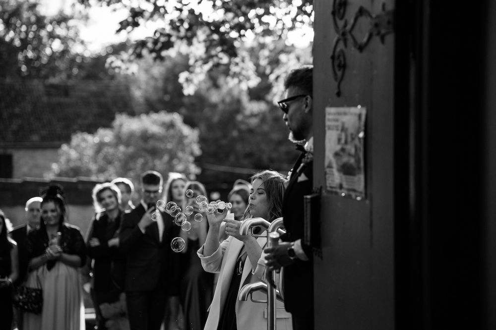 Black and white photo of wedding guests blowing bubbles outside church after ceremony.