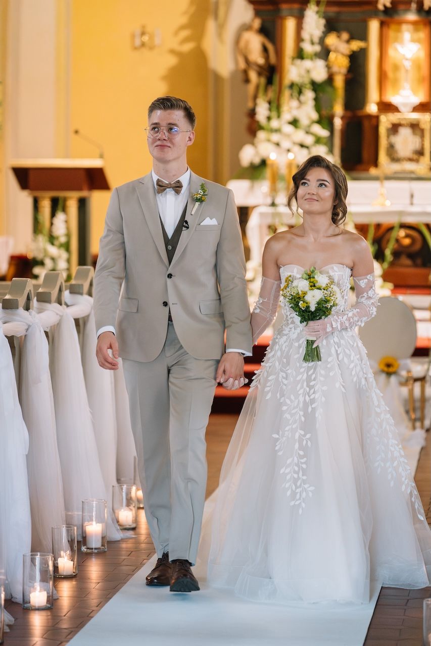 Bride and groom walking down candlelit church aisle after wedding ceremony holding hands.