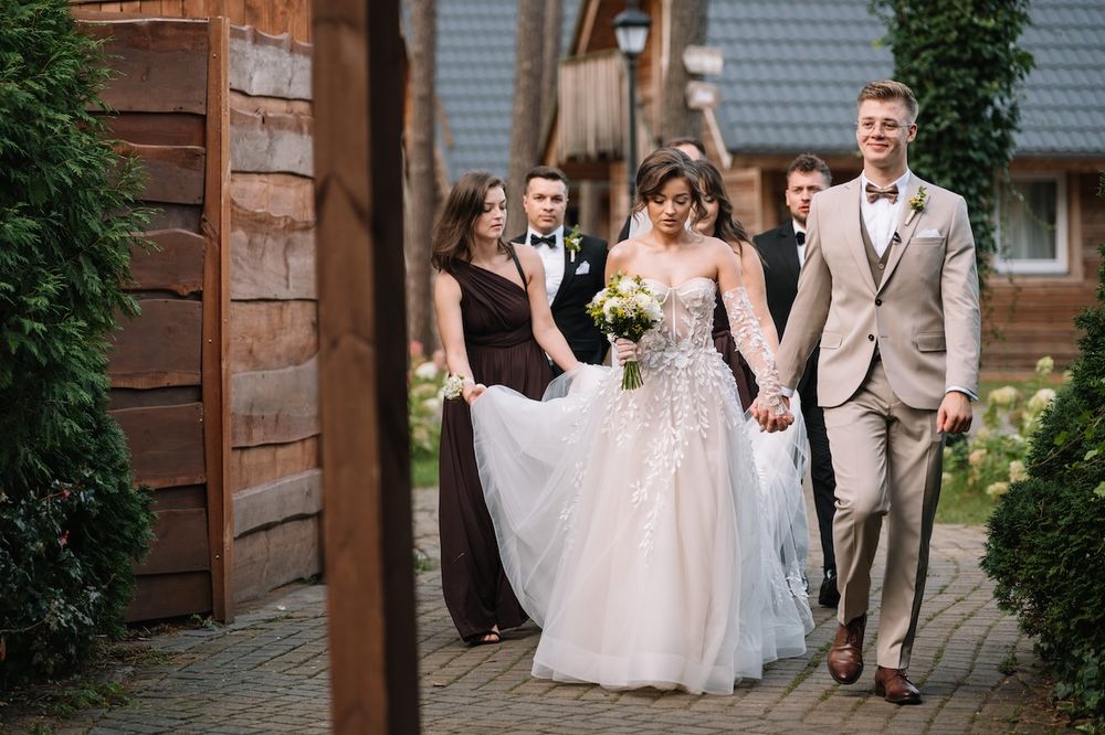 Bride and groom walk hand in hand with wedding party along rustic cobblestone path.