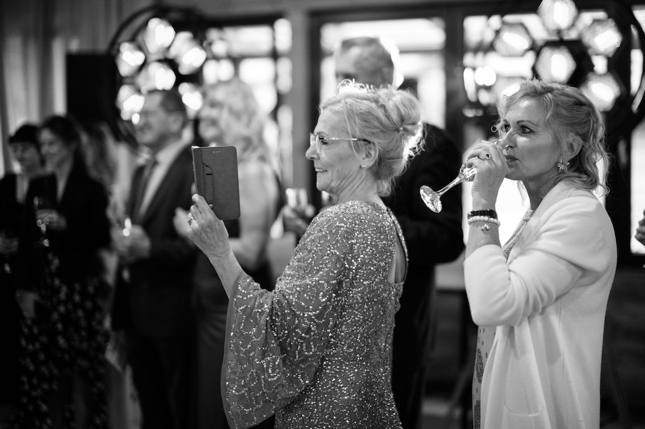 Black and white photo of wedding guests, one holding tablet to capture ceremony moment.