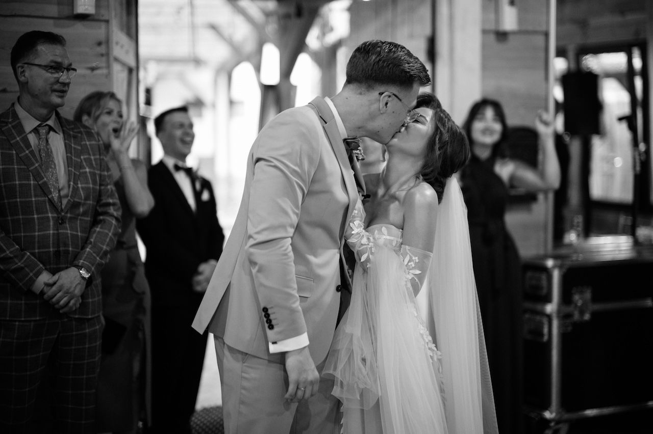 Black and white photo of newlyweds sharing romantic first kiss at wedding ceremony.