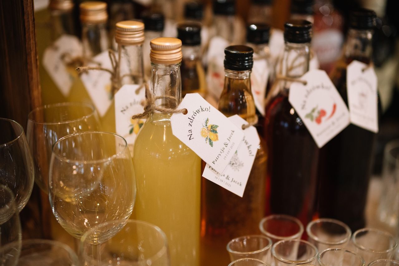 Decorative wedding favor bottles with personalized tags displayed on wooden shelf at reception.