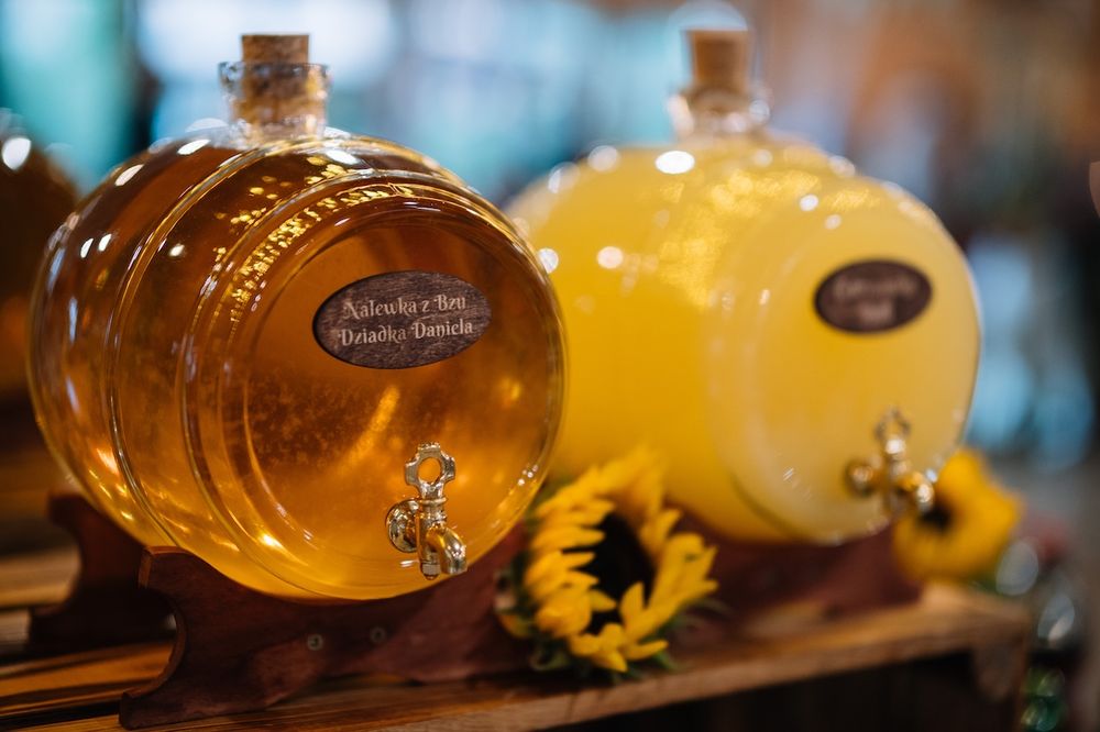 Two large glass drink dispensers with custom labels and sunflower decoration at wedding reception.