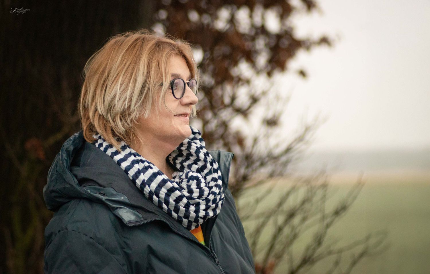 Natürliches Outdoor-Portrait einer Frau im Profil mit Brille und Schal vor herbstlicher Landschaft