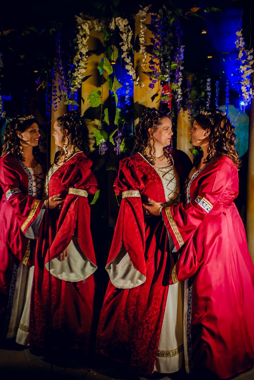A group of performers in red robes stand together during a dramatic nighttime theatrical performance with blue lighting.