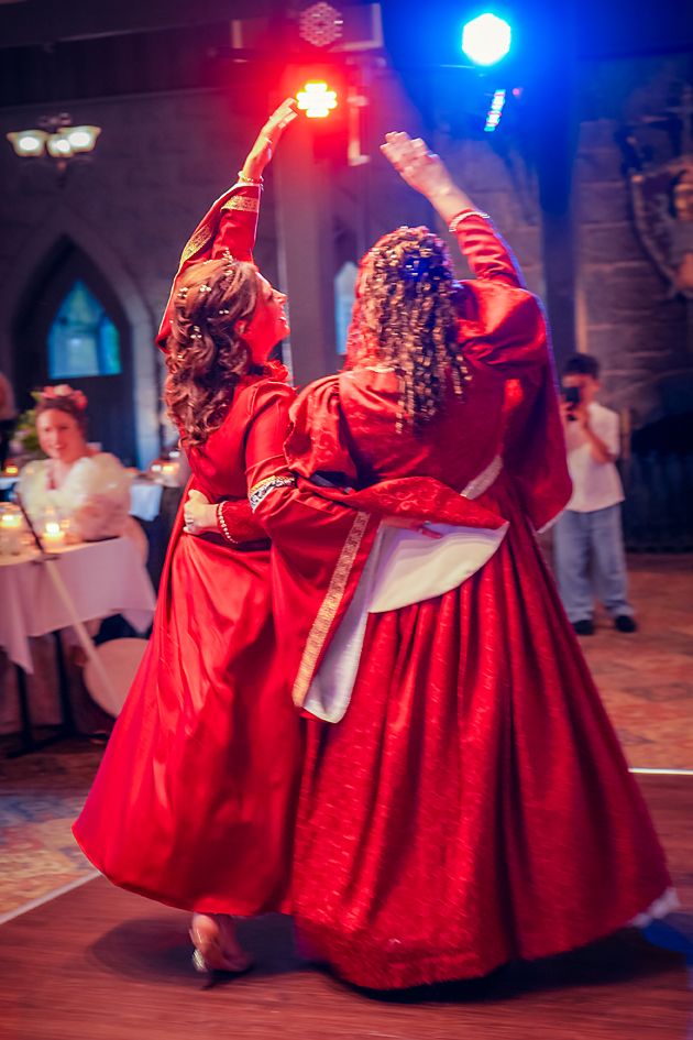 Two dancers in flowing red gowns perform with raised arms under colorful stage lighting at an indoor event.
