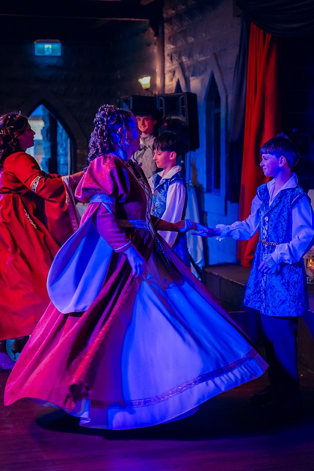 Dancers in flowing period dresses perform under dramatic red and blue stage lighting during a traditional ballroom show.