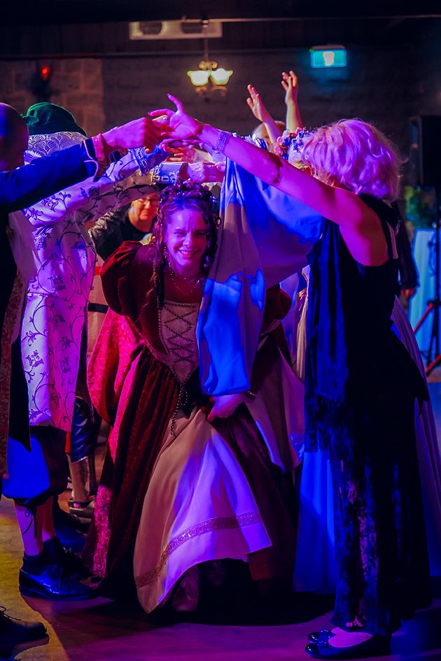 Silhouettes of dancers moving under vibrant purple and blue stage lighting at a social dance event.
