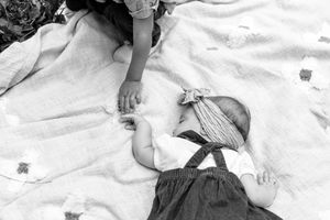 Black and white photograph of a sleeping baby wearing overalls lying on a floral patterned blanket.