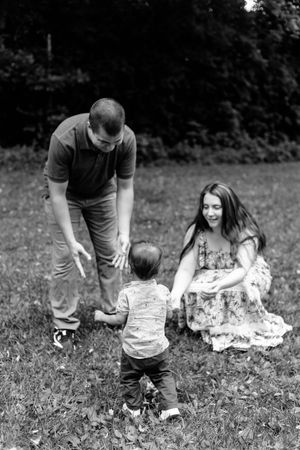 Black and white photo of a family playing together on grass with trees in background.