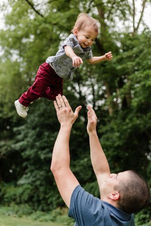 A sequence showing a playful moment as a small child is tossed in the air against a green outdoor background.