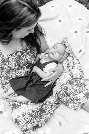 Black and white photo of a mother and sleeping baby on a polka dot blanket outdoors.