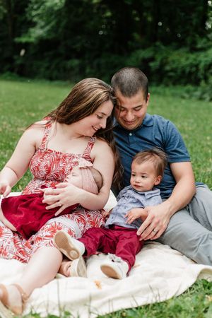 Family relaxes together on a picnic blanket in a grassy outdoor setting.