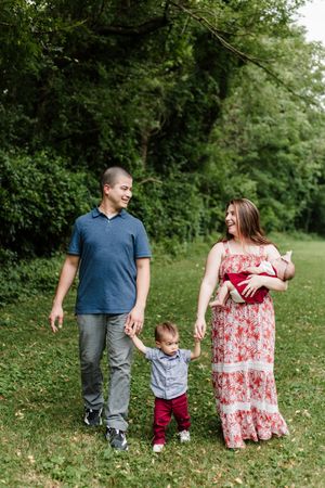 Family walking together outdoors with toddler holding parents' hands on a summer day.