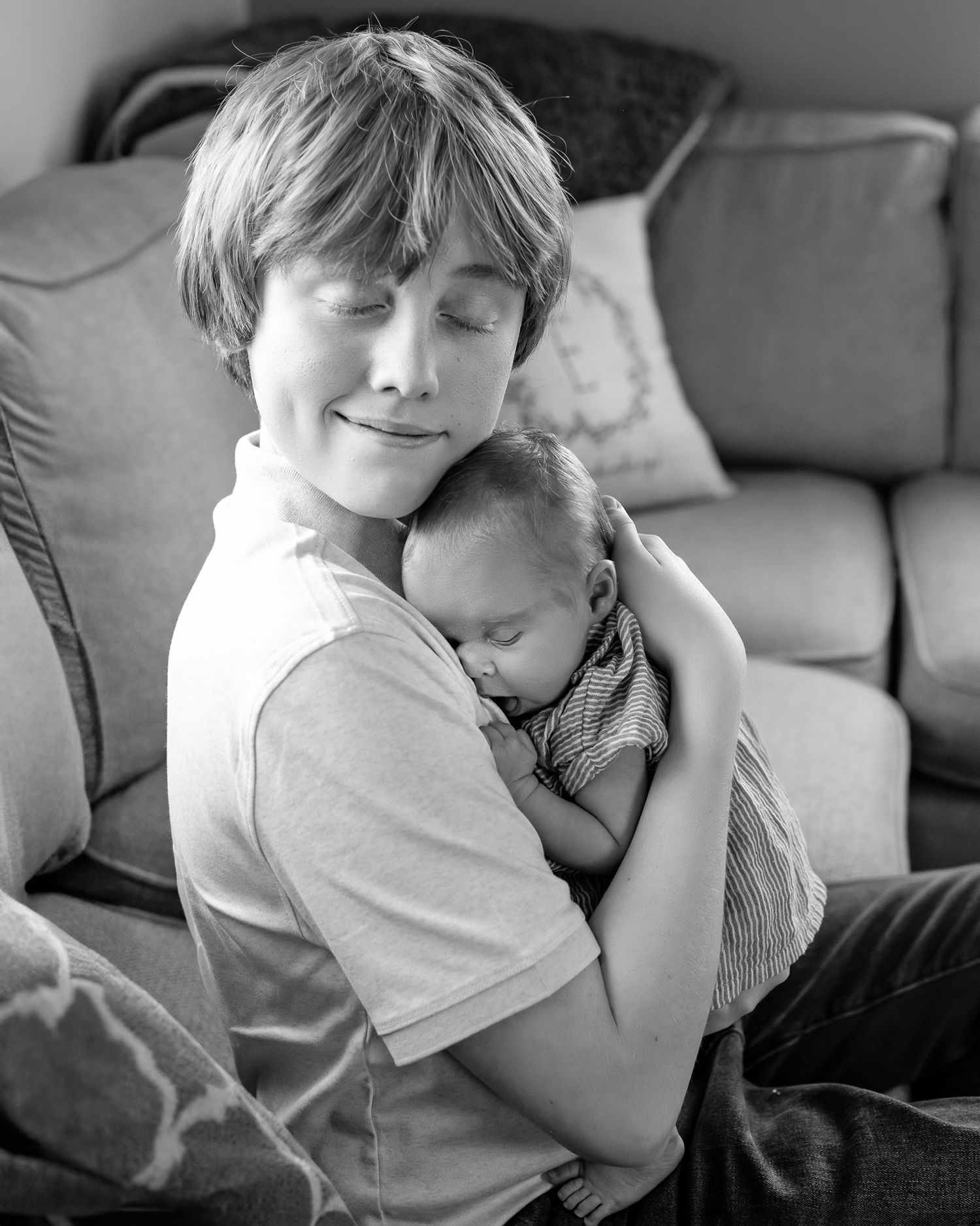 An older brother holding his newborn sister on the couch during an in-home photoshoot.