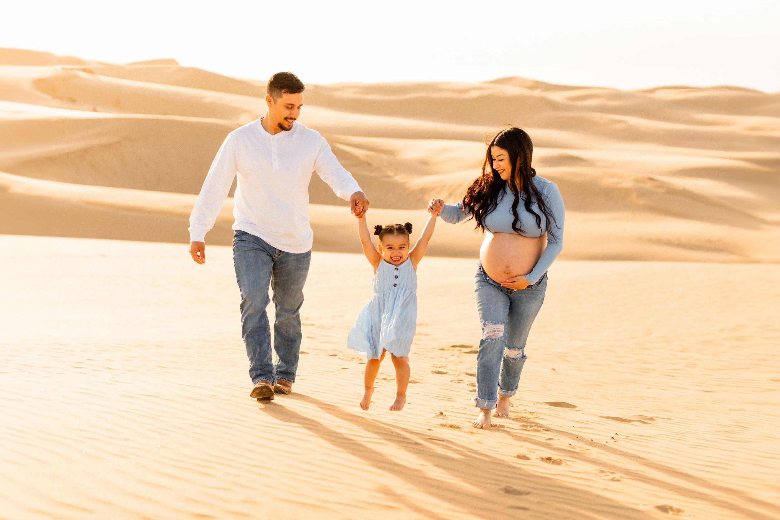 A family plays together while walking through rolling sand dunes at sunset.