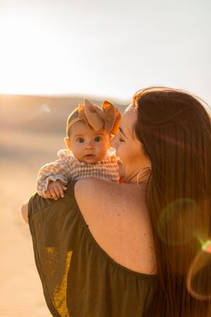 Parent holds baby wearing bow headband during sunset photoshoot.