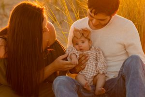 A family enjoys a tender moment together in golden sunset light while sitting in tall grass.