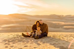 A family sits together on desert sand dunes during a golden sunset.