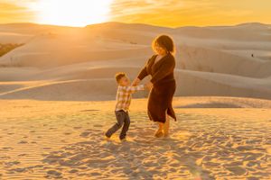 Two people play together on sandy dunes against a vibrant orange sunset sky.