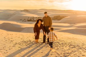 A family walks together across scenic sand dunes at sunset creating long shadows.
