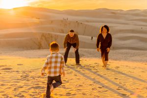 A small group runs and plays on sand dunes during golden hour.