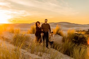 A family stands together in tall grass with sand dunes and sunset in background.