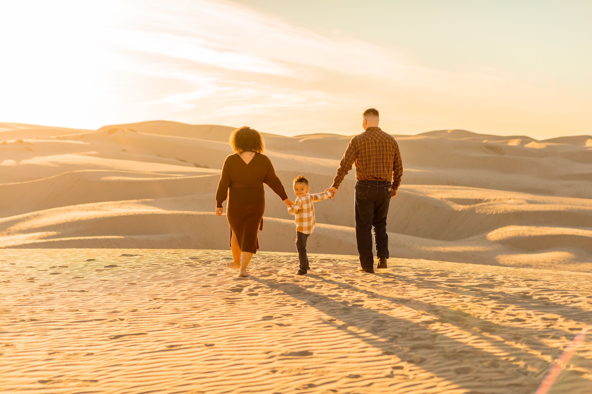 Three people walk hand in hand across desert sand dunes at sunset.