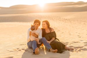 Family sits together on sandy dunes during golden hour photoshoot.