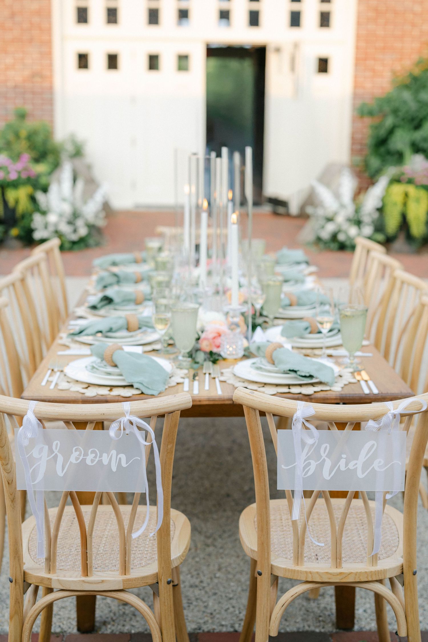 Wooden chairs with white signs at an elegant outdoor table setting on brick patio with turquoise accents. - Elawa Farm