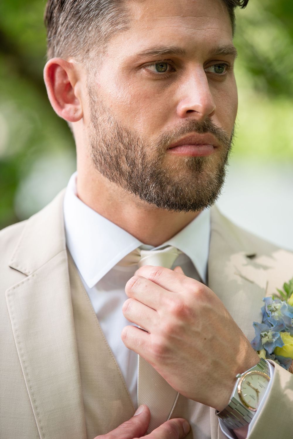 Close-up profile shot of groom adjusting tie with boutonnière on lapel.